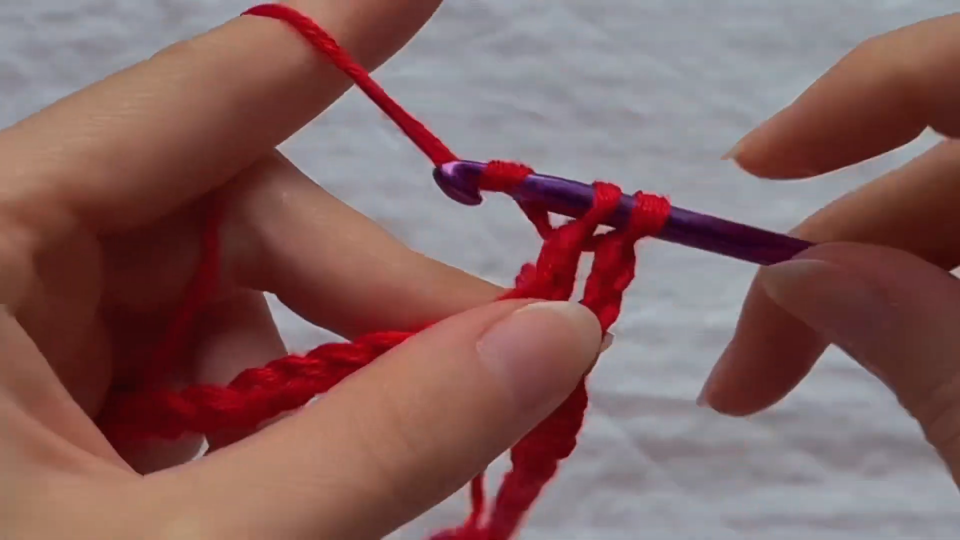 Crochet hook pulling red yarn through stitches to build fabric