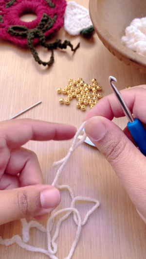 Crocheting a foundation chain with white yarn beside gold beads.