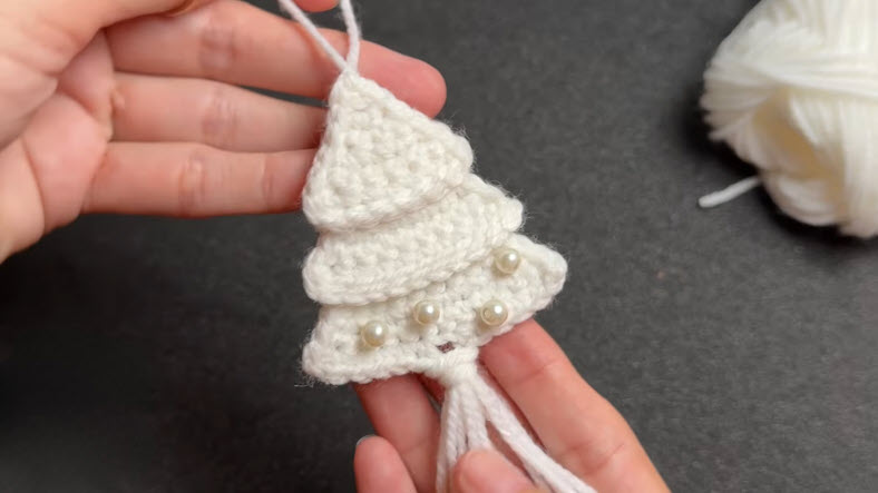 Finished white crochet tree with pearls and hanging yarn tassels.