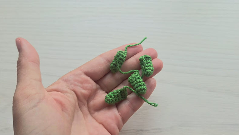 Four green crochet toad legs on open hand