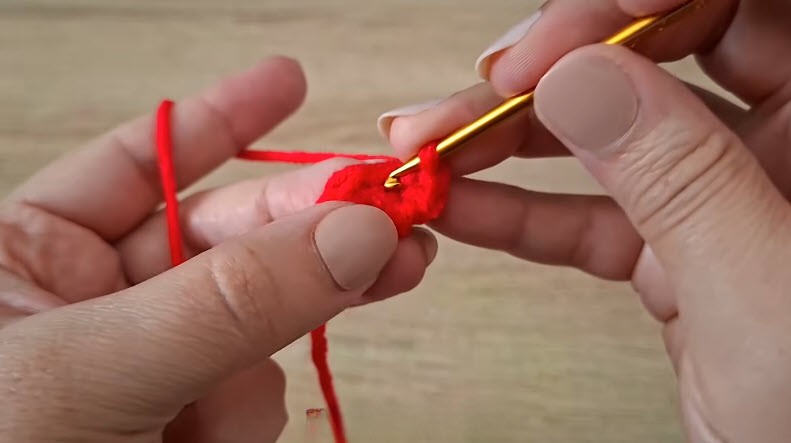 Hands crocheting into red yarn with gold hook.