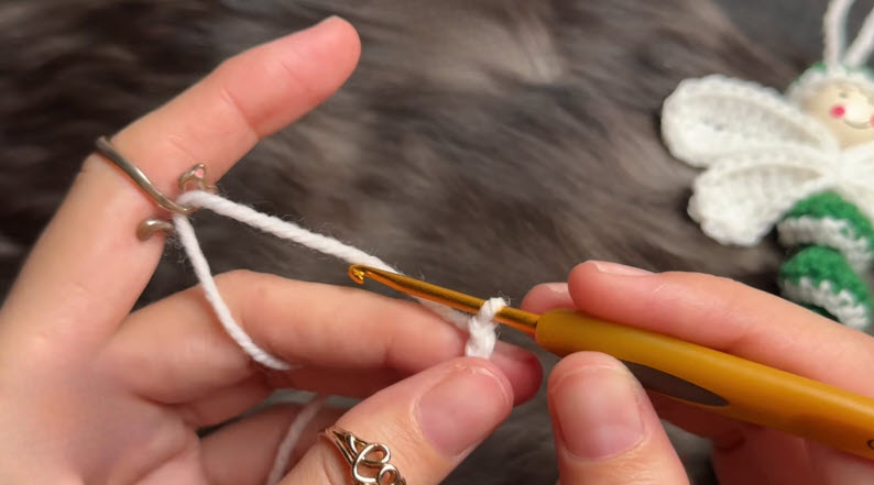 Hands starting a magic ring with white yarn and gold crochet hook.