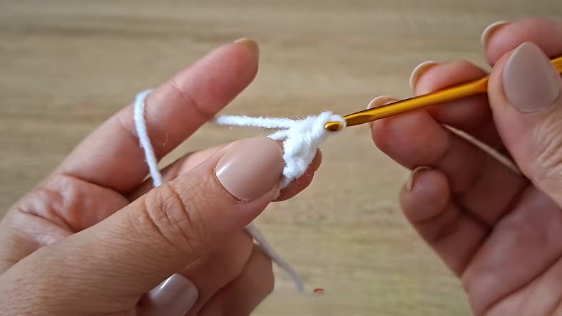 Hands starting a magic ring with white yarn and gold crochet hook.