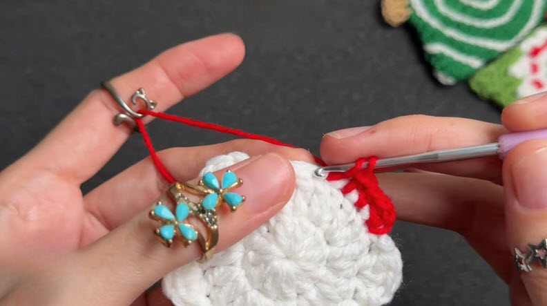 Hook making half double crochet stitches with red yarn edging.