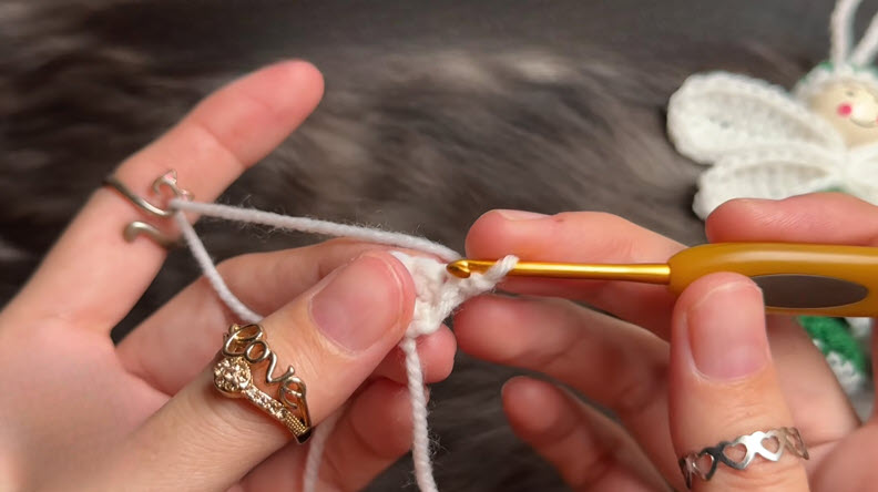 Hook pulling white yarn through the first crochet loop.
