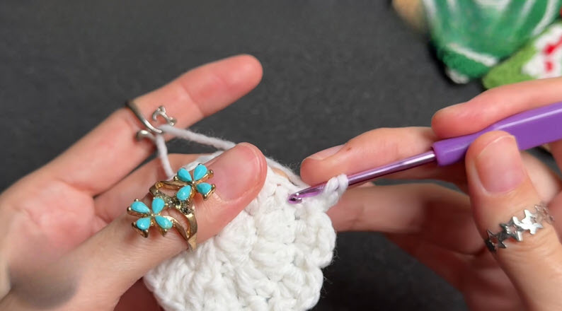 Purple hook crocheting shell stitches into a white round.