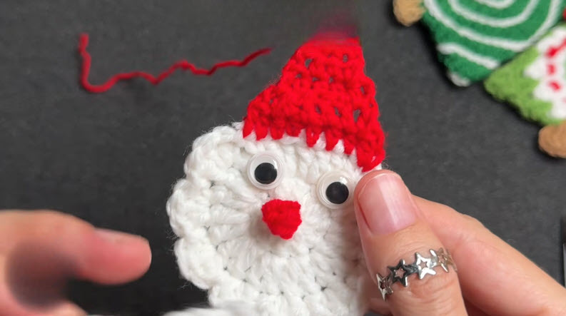 Santa face with googly eyes and red nose being glued on.