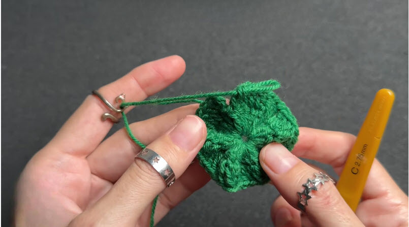 Tightening the center hole of a green crochet piece.