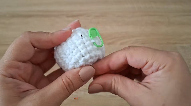White crochet ball with green locking stitch marker.