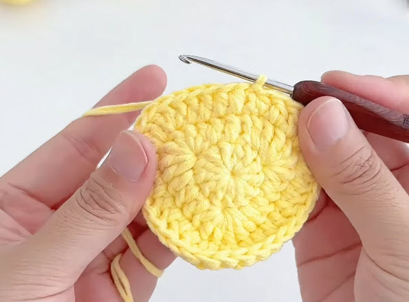 Working rows to shape a yellow crochet circle.