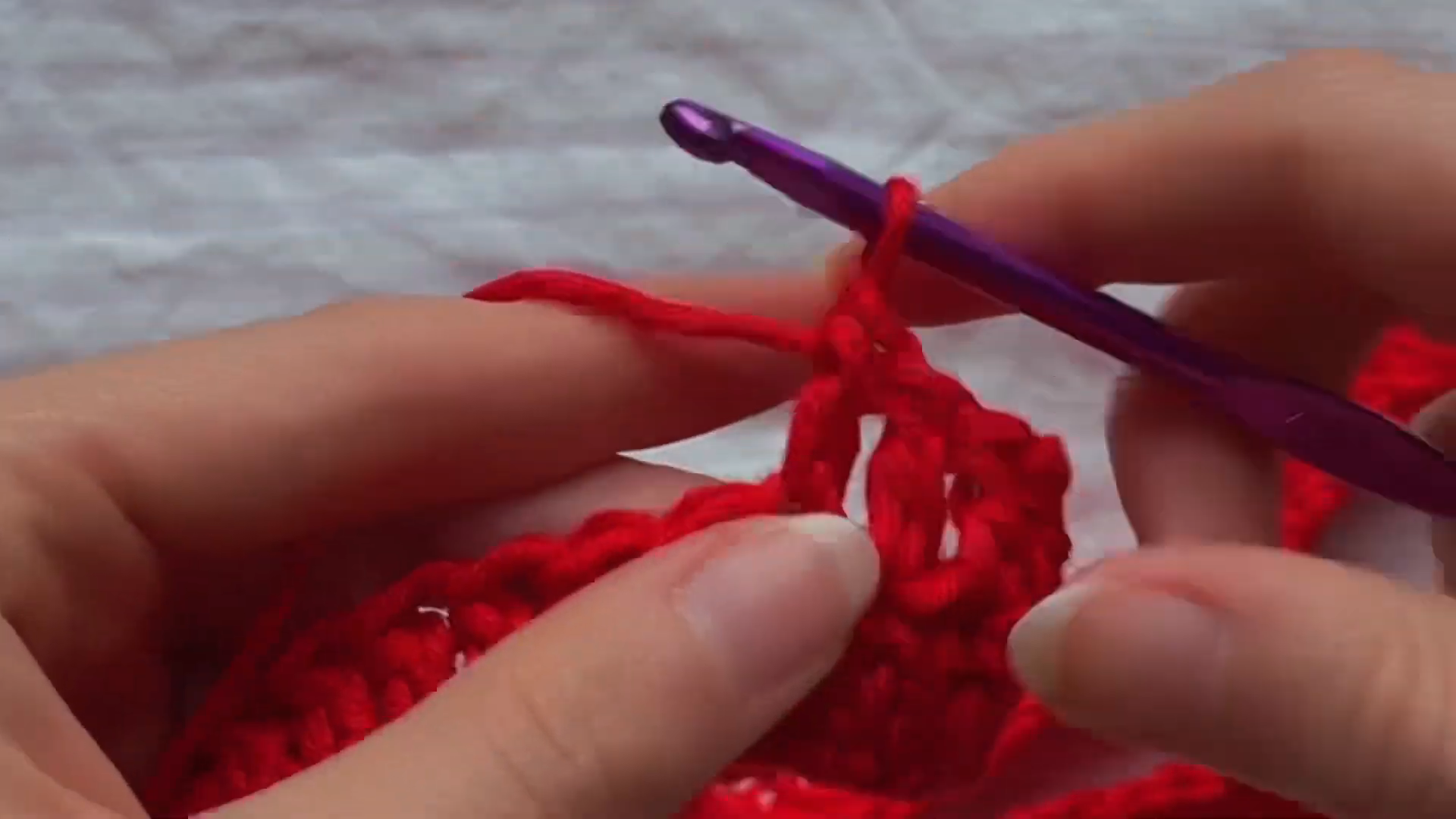 Working single crochet stitches into red yarn fabric edge