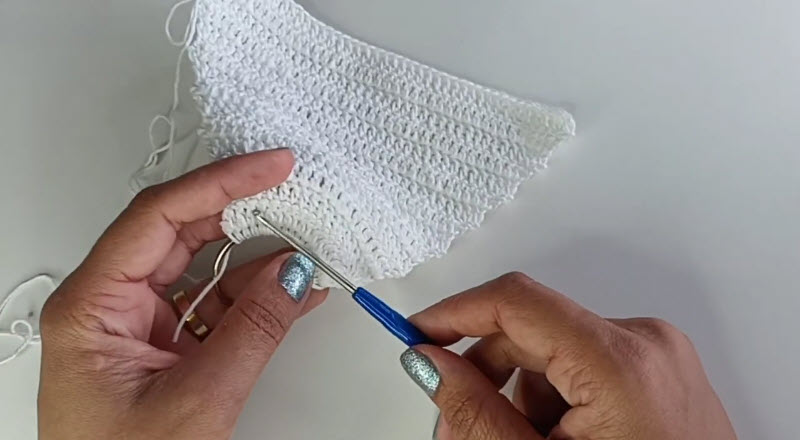 Working the edge stitches on a triangular white piece.