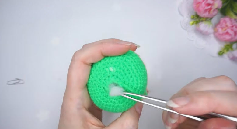 Adding white stuffing into the green crochet budgie body with tweezers.