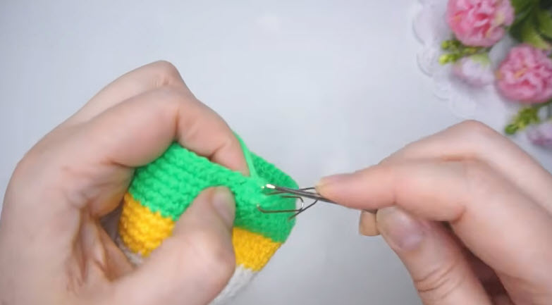 Closing the yellow and green crochet budgie piece with a hook before stuffing.