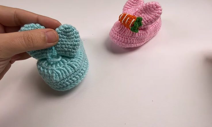 Finished blue crochet bunny baby shoes with two fluffy ears on the front.