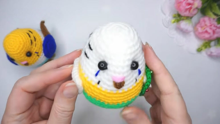 Finished white, yellow and green crochet budgie with a blue-cheeked friend behind.