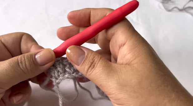 Holding the gray piece with the red hook resting on top of the work.