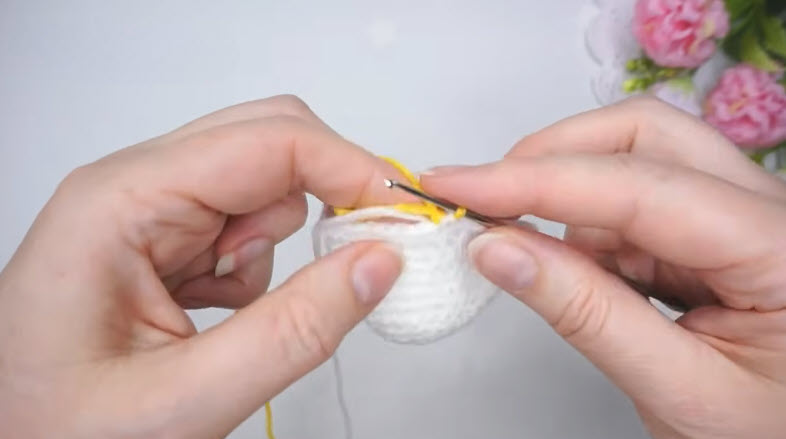 Joining yellow yarn to the white rounded crochet budgie body.
