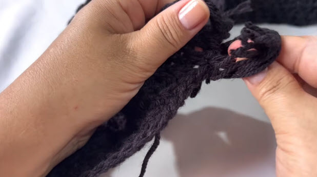 Pulling black yarn strands through the edge to make the fringe.