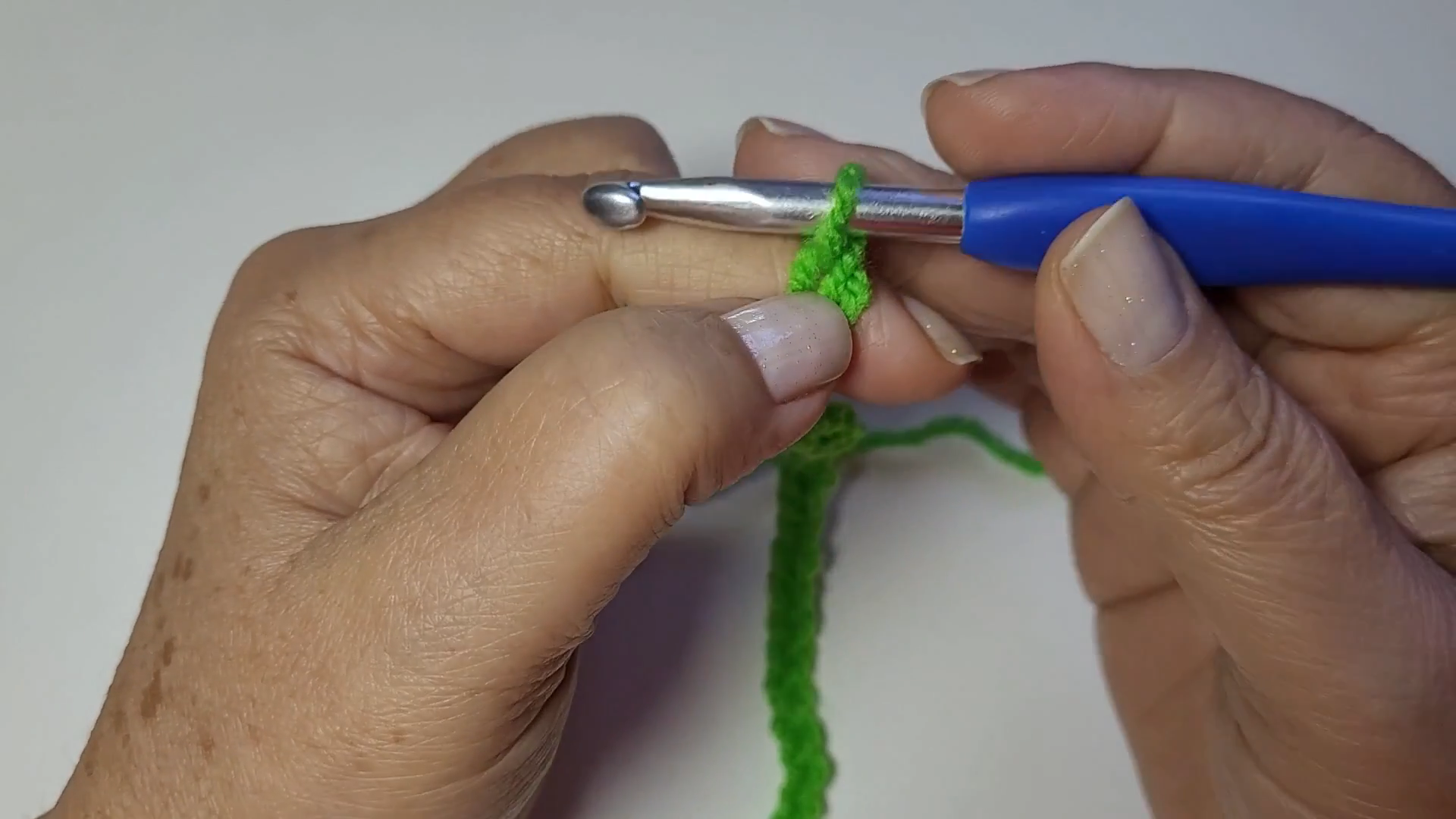 Starting the foundation chain for the crochet cardigan with green yarn and a blue hook