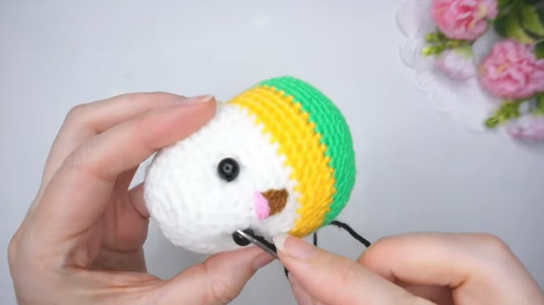 Stitching the black eye and beak onto the white face of the crochet budgie.