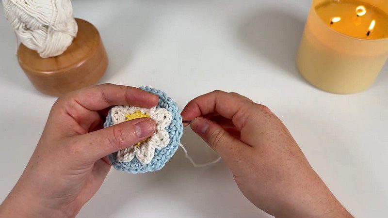 White daisy sewn onto the blue base of the daisy car coaster crochet
